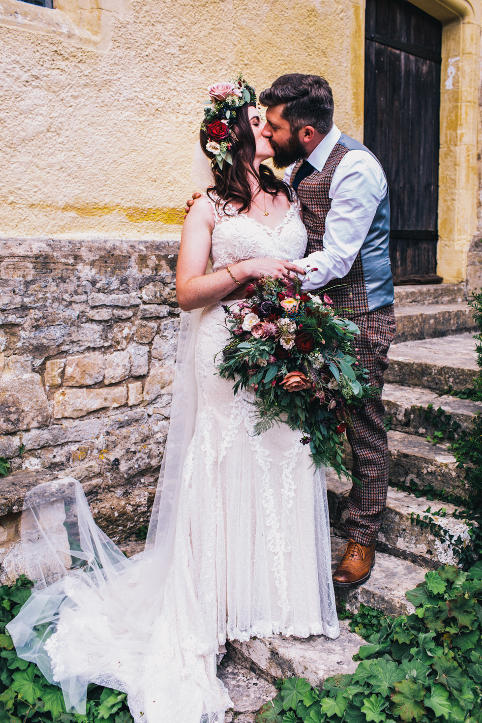 quirky bride and groom kissing against yellow stone wall at Owlpen Manor