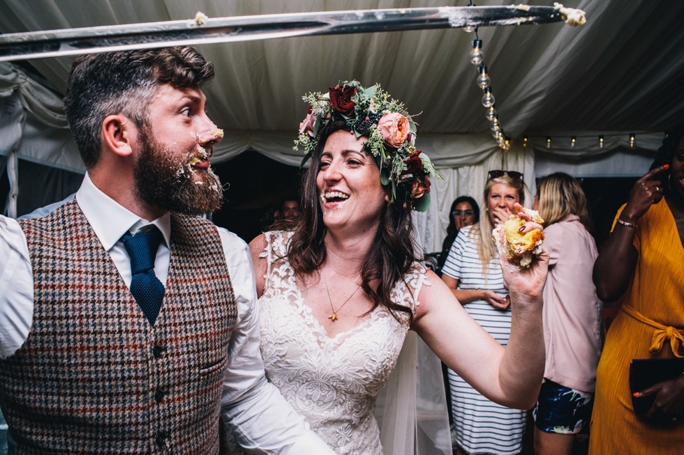 bride shoving cake into grooms face at fun filled festival wedding at Owlpen Manor