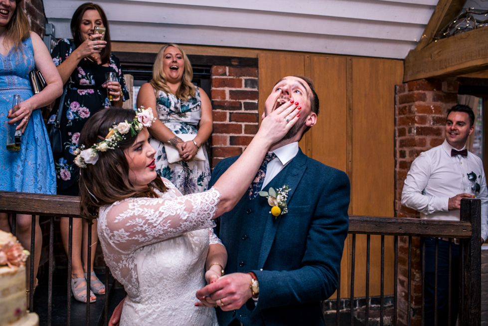 bride feeding wedding cake to groom by shoving it in his face