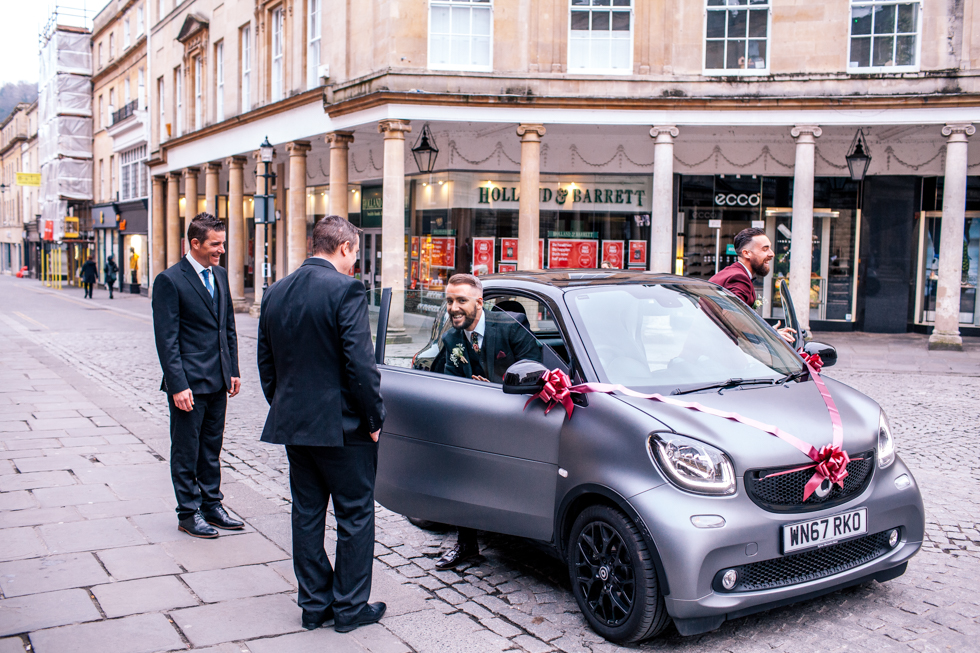 Groom and groom arriving in decorated smart car at wedding