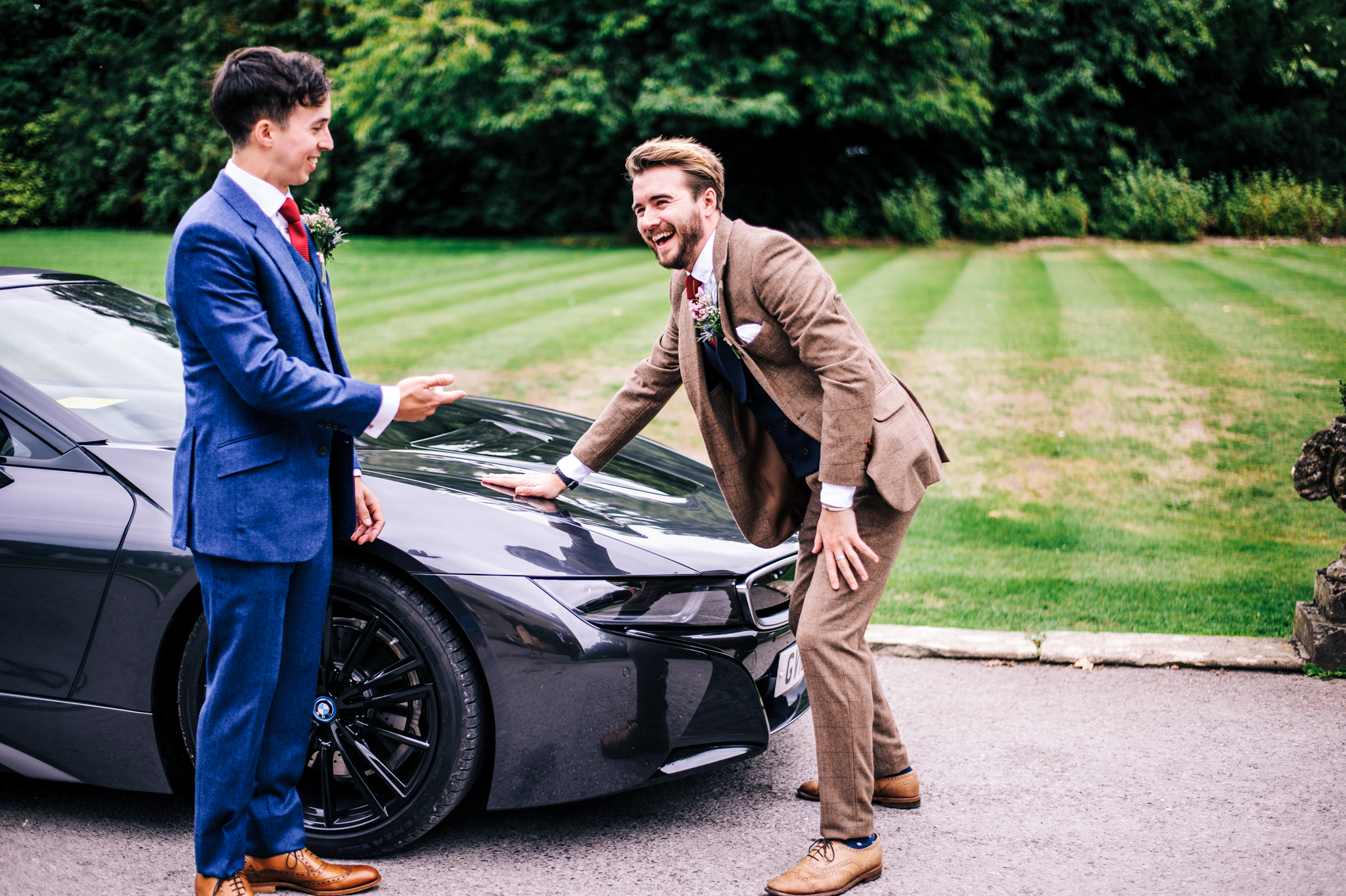 Groom and best man laughing next to sports car at Babbington House