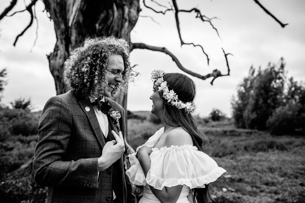 couple portrait of bohemian bride and long haired groom walking through fields at festival wedding