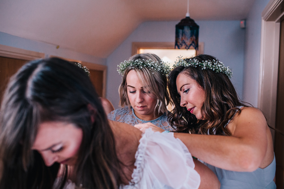 bridesmaids helping bride to fasten wedding dress