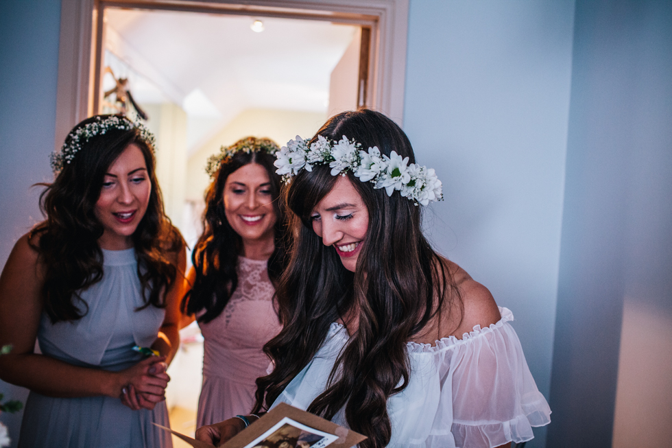 bride opening gift from groom on morning of wedding wearing flower crown and charity shop wedding dress