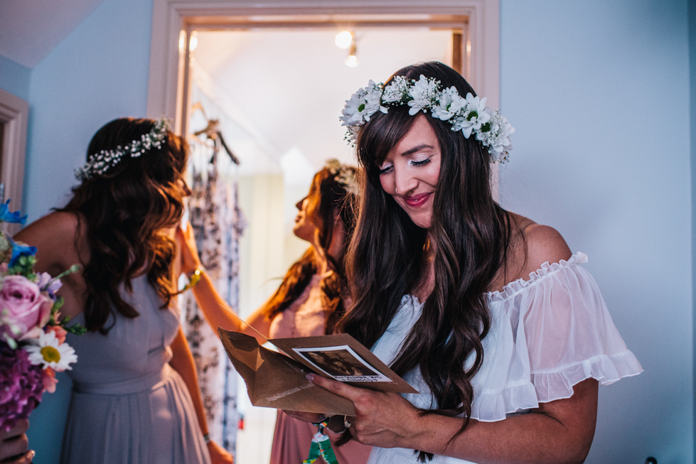 bride opening gift from groom on morning of wedding wearing flower crown and charity shop wedding dress