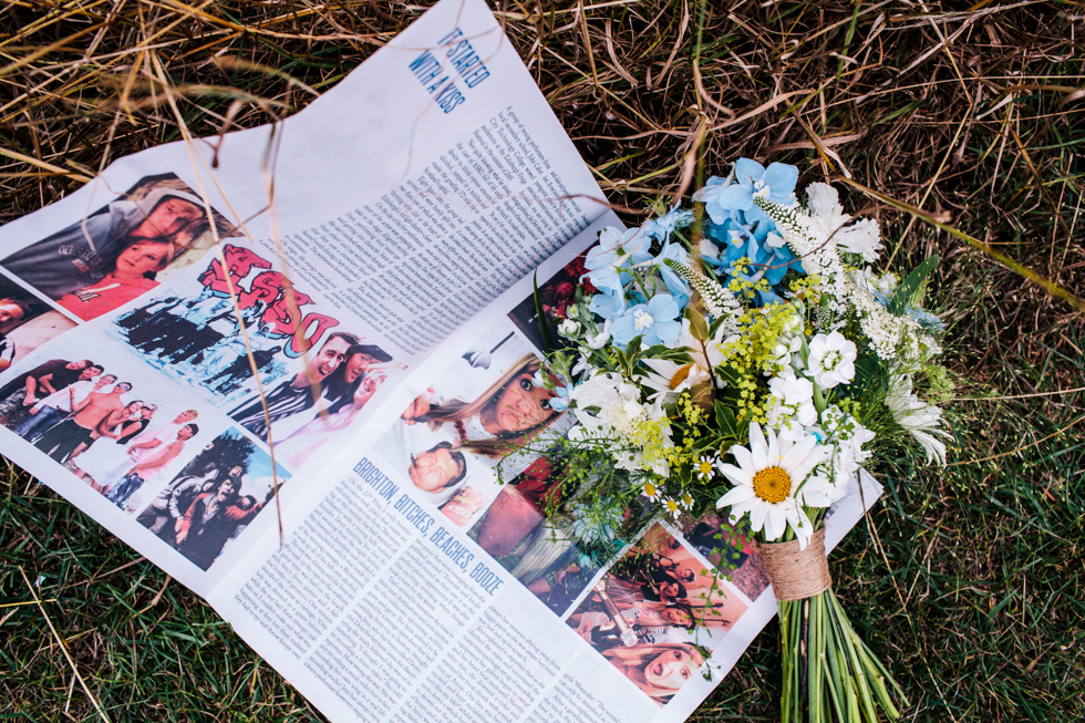 Couples hand made wedding newspaper next to rustic flowers at Quantock Lakes