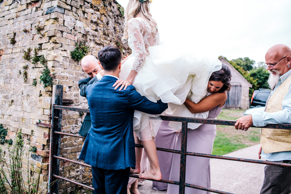 groom carrying bride over fence at wall garden Mells