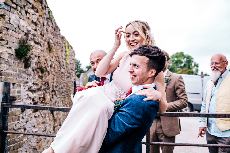 bridesmaid being carried by groom over fence for group shots