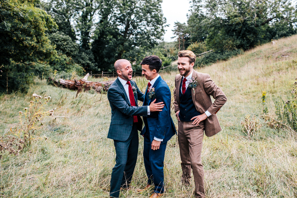 groom best man and usher laughing and messing about in a field for their own special photo at wedding near Mells frome